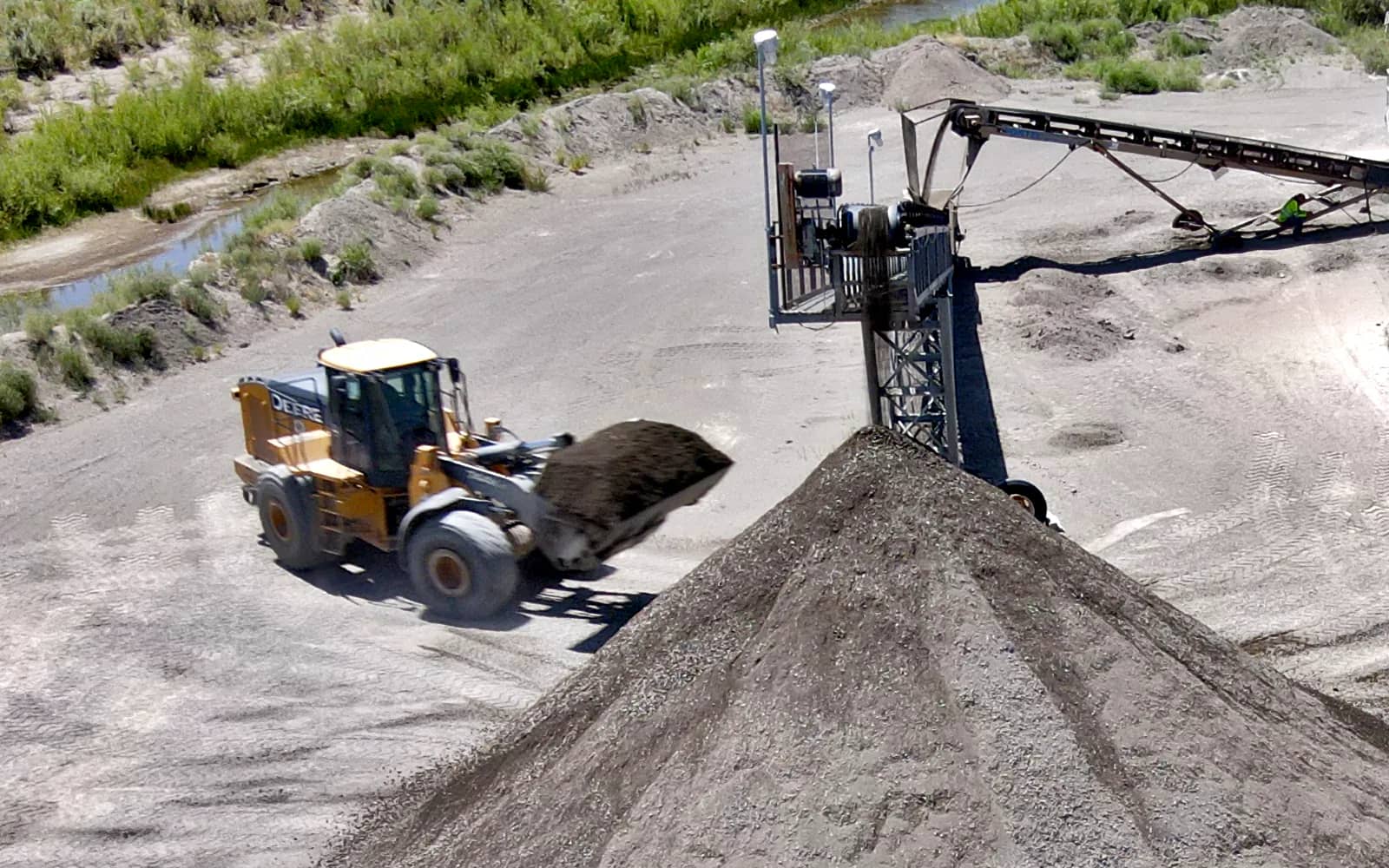 Loader working near conveyor moving material into stockpile