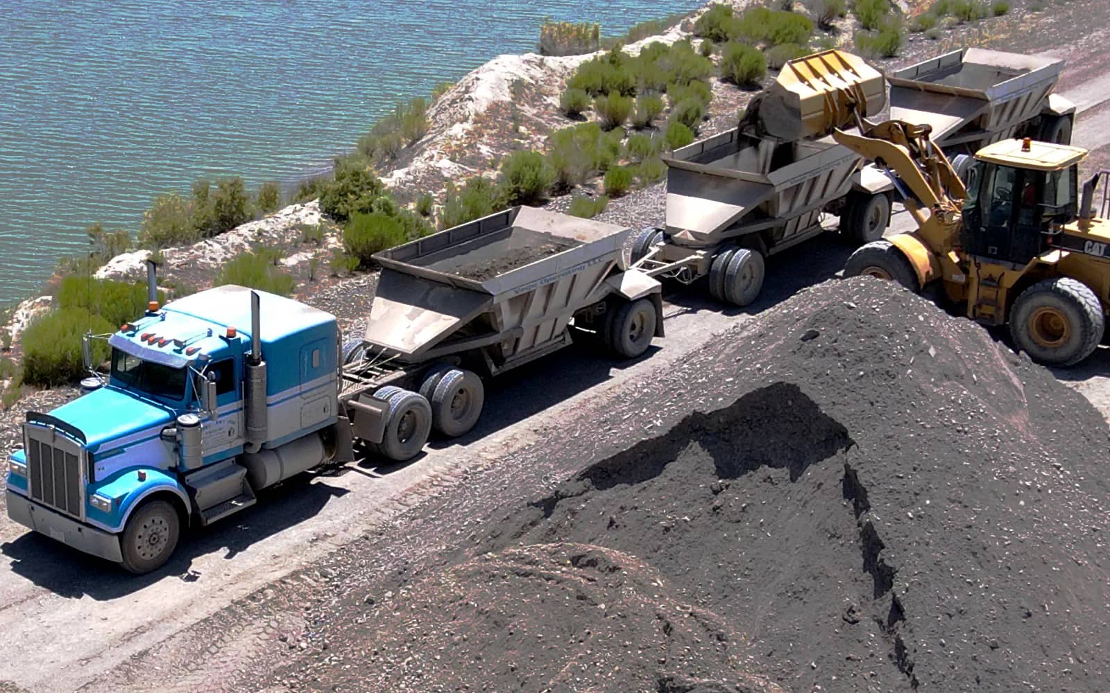 Loader filling belly dump truck with scraped material